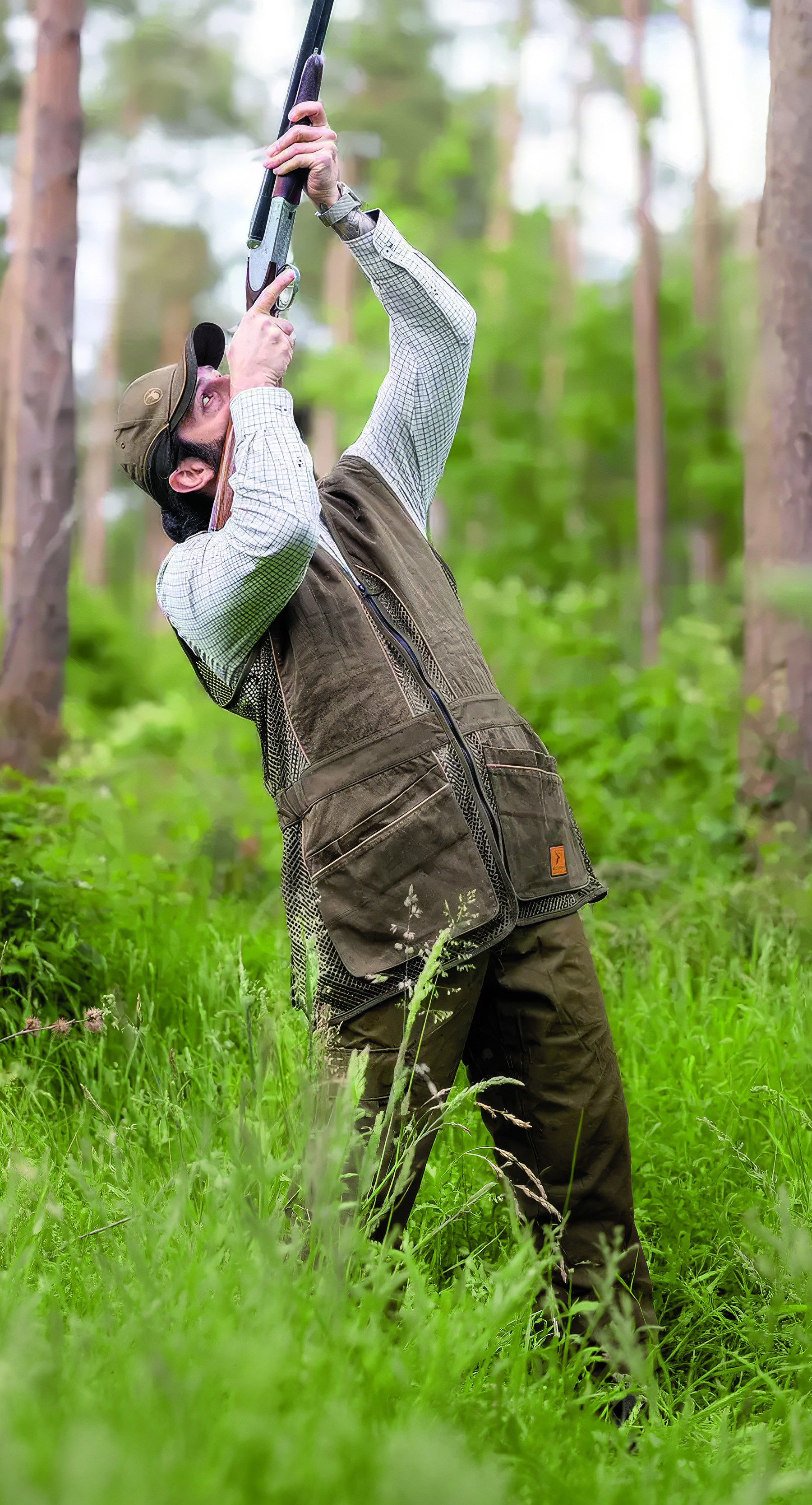 Clay shooter wearing the New Forest Skeet vest while shooting overhead targets in a woodland setting