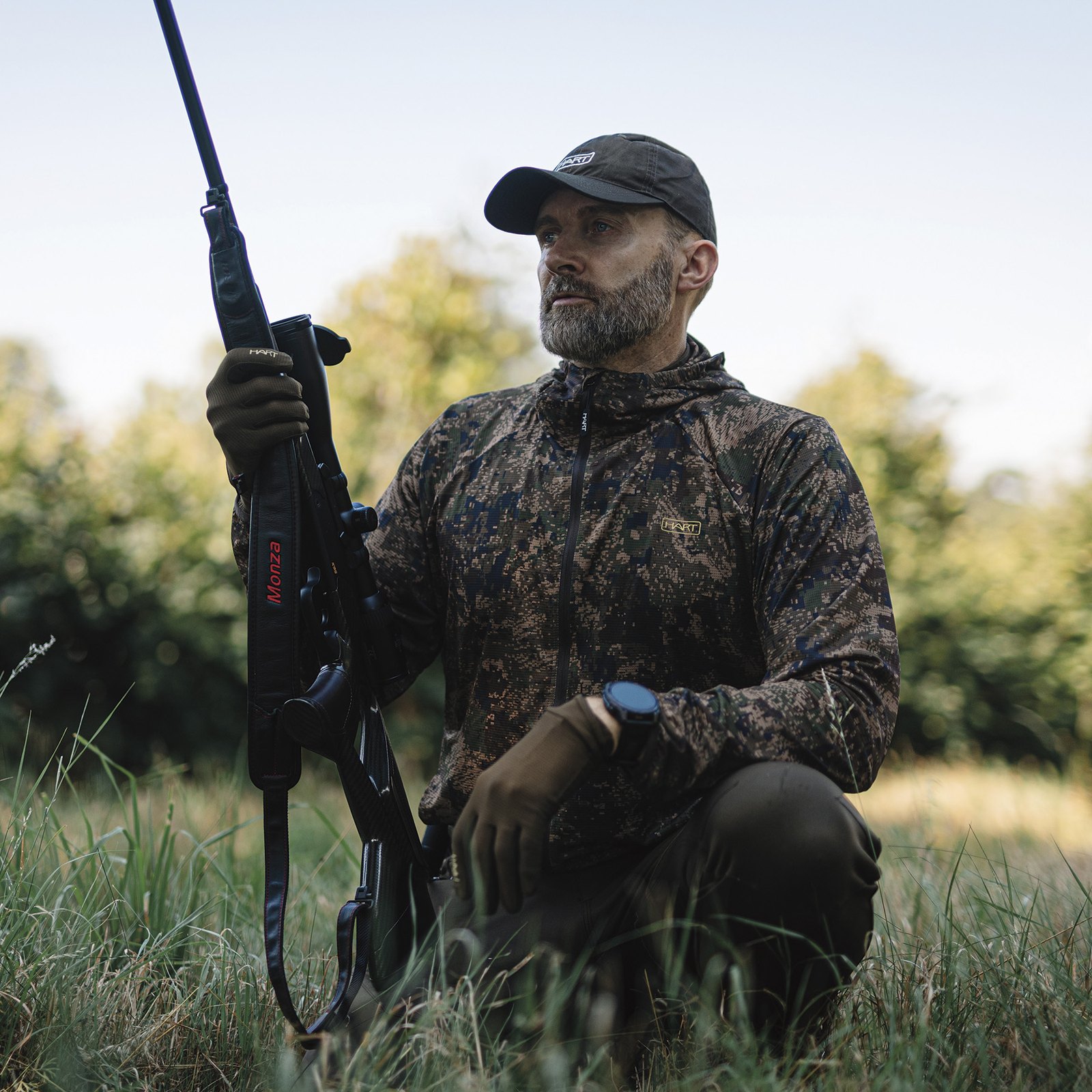 Stalker in HART camouflage kneeling in cover with a moderated rifle while stalking deer