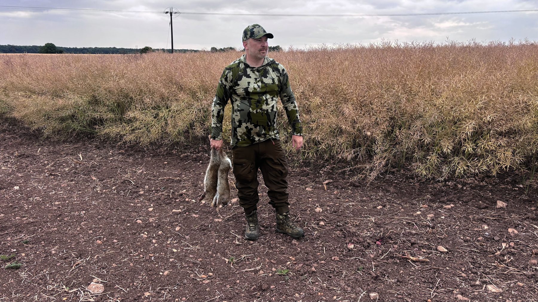 Danny Brookfield holding a rabbit taken with an air rifle beside a field of oilseed rape