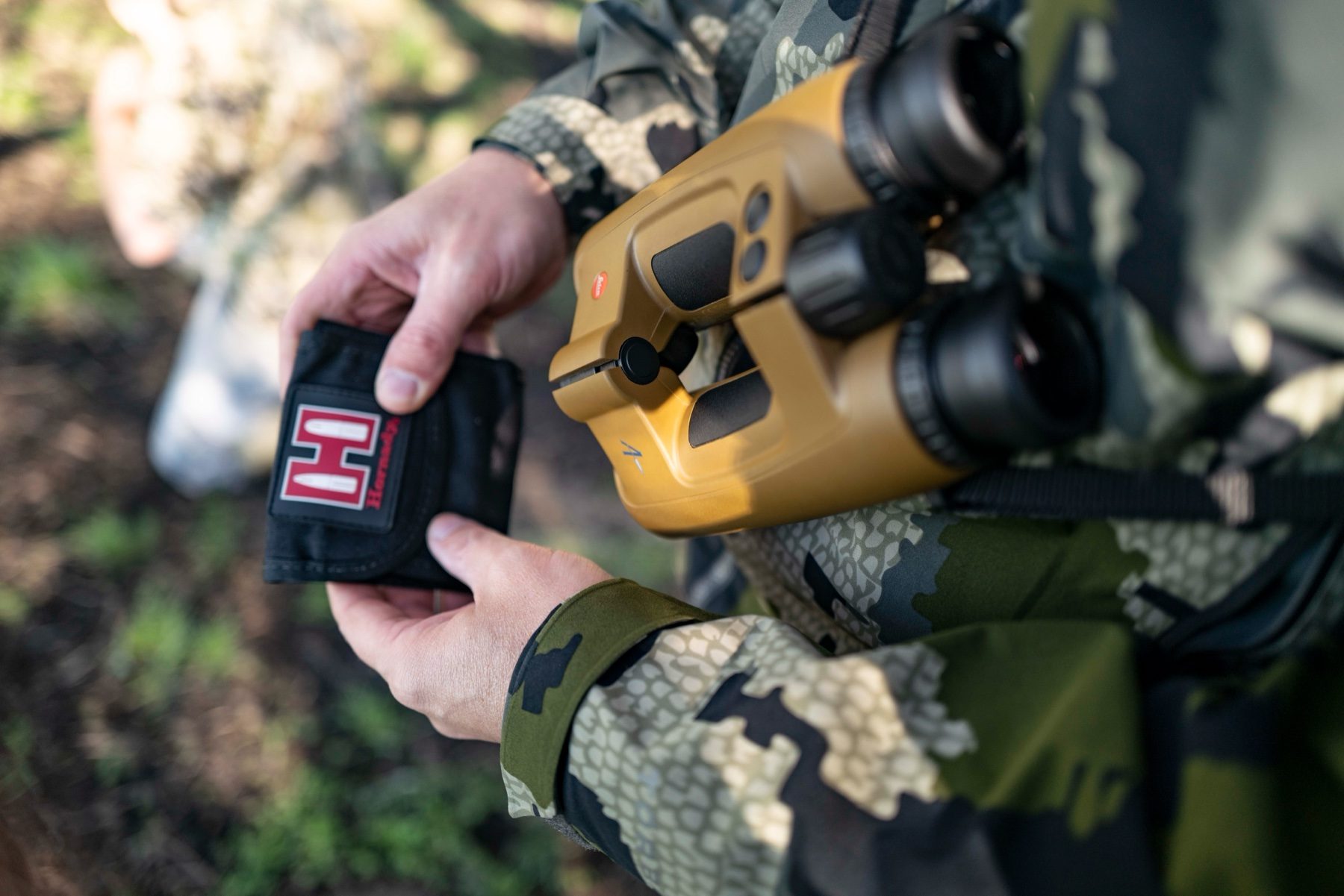 A hunter holding a Hornady ammunition wallet and Leica Geovid Pro rangefinding binoculars