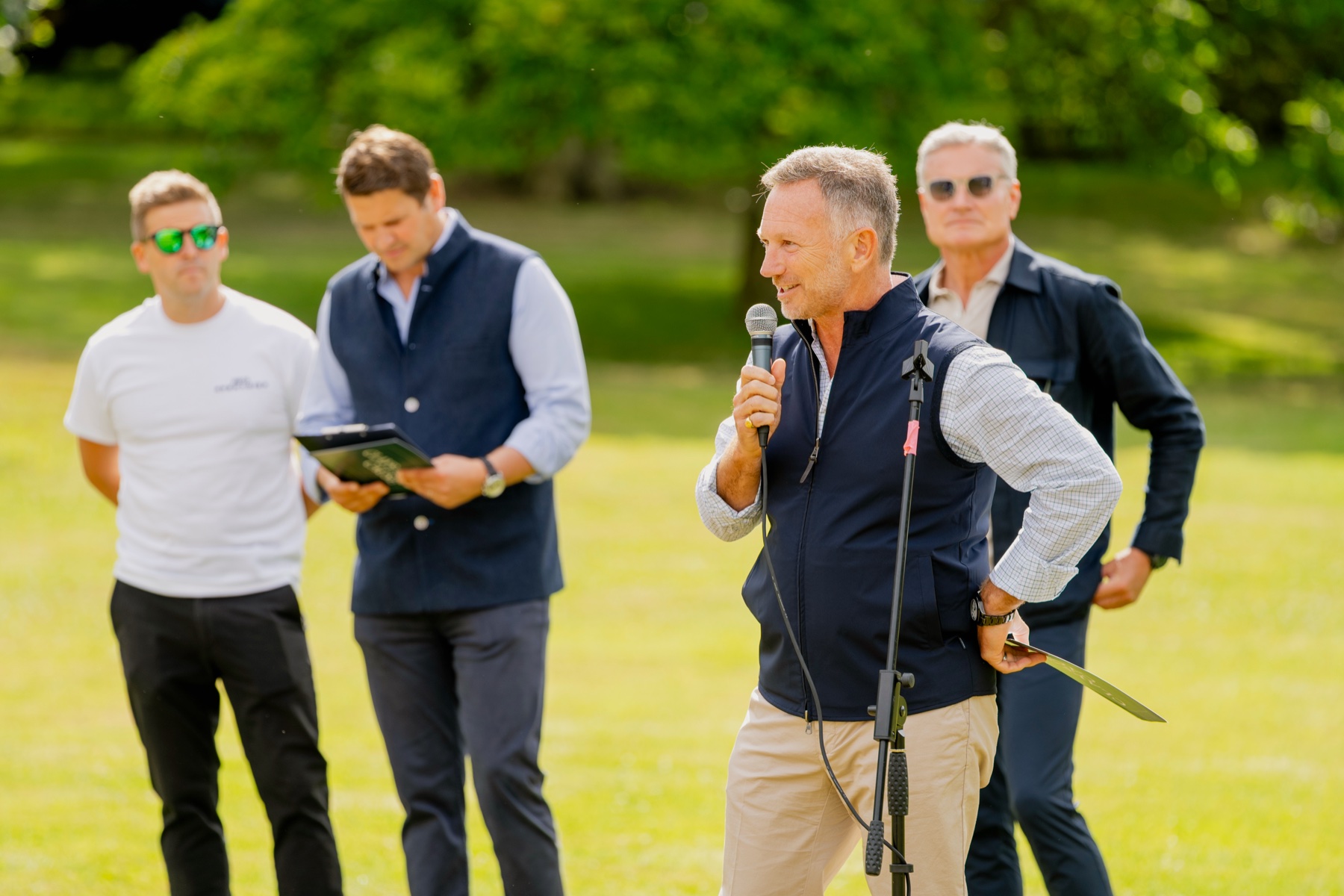 Christian Horner speaking on a microphone at Clays for a Cause with David Coulthard behind him