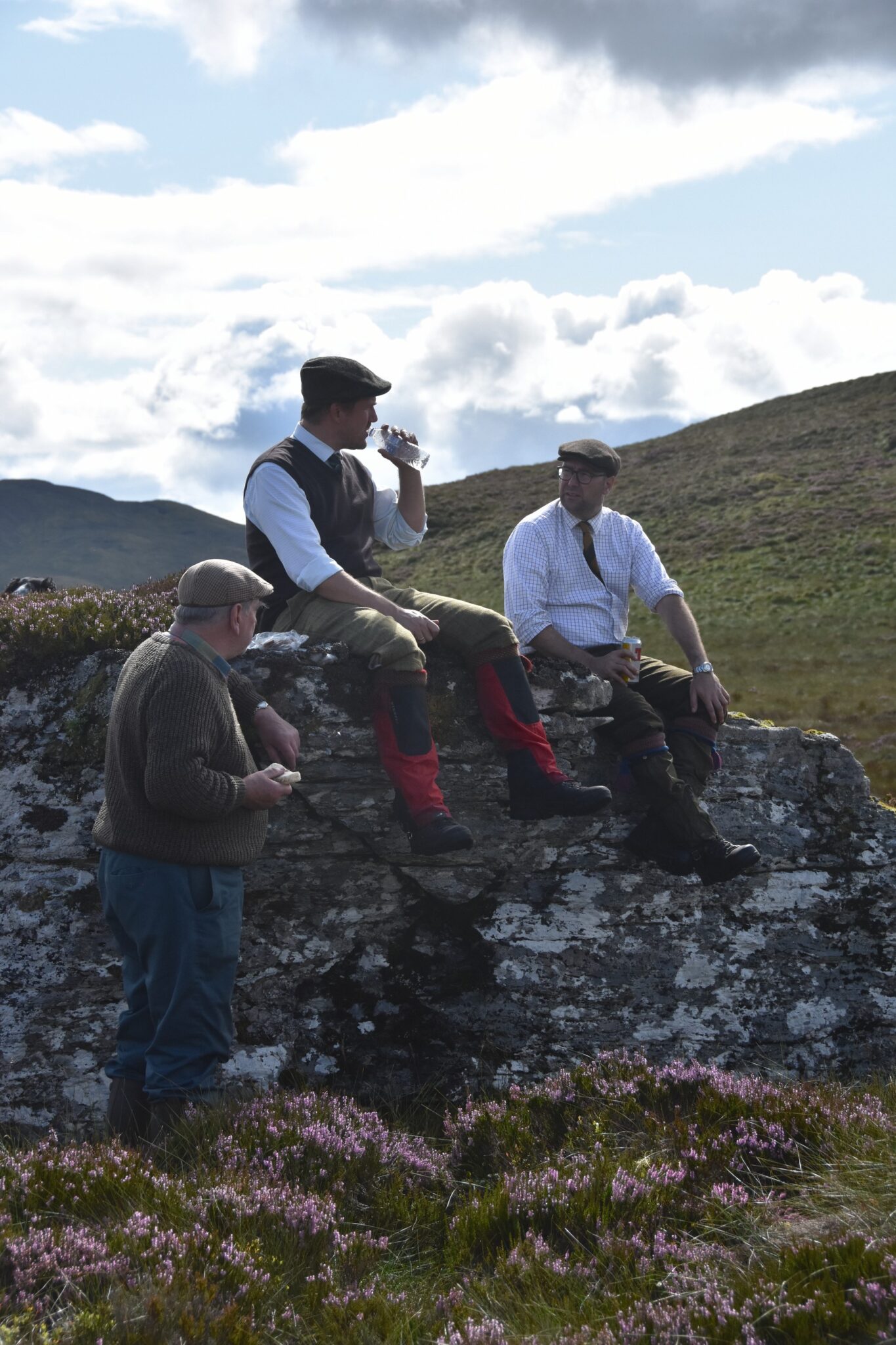 Four members of a grouse shooting party resting on a rocky outcrop at lunchtime