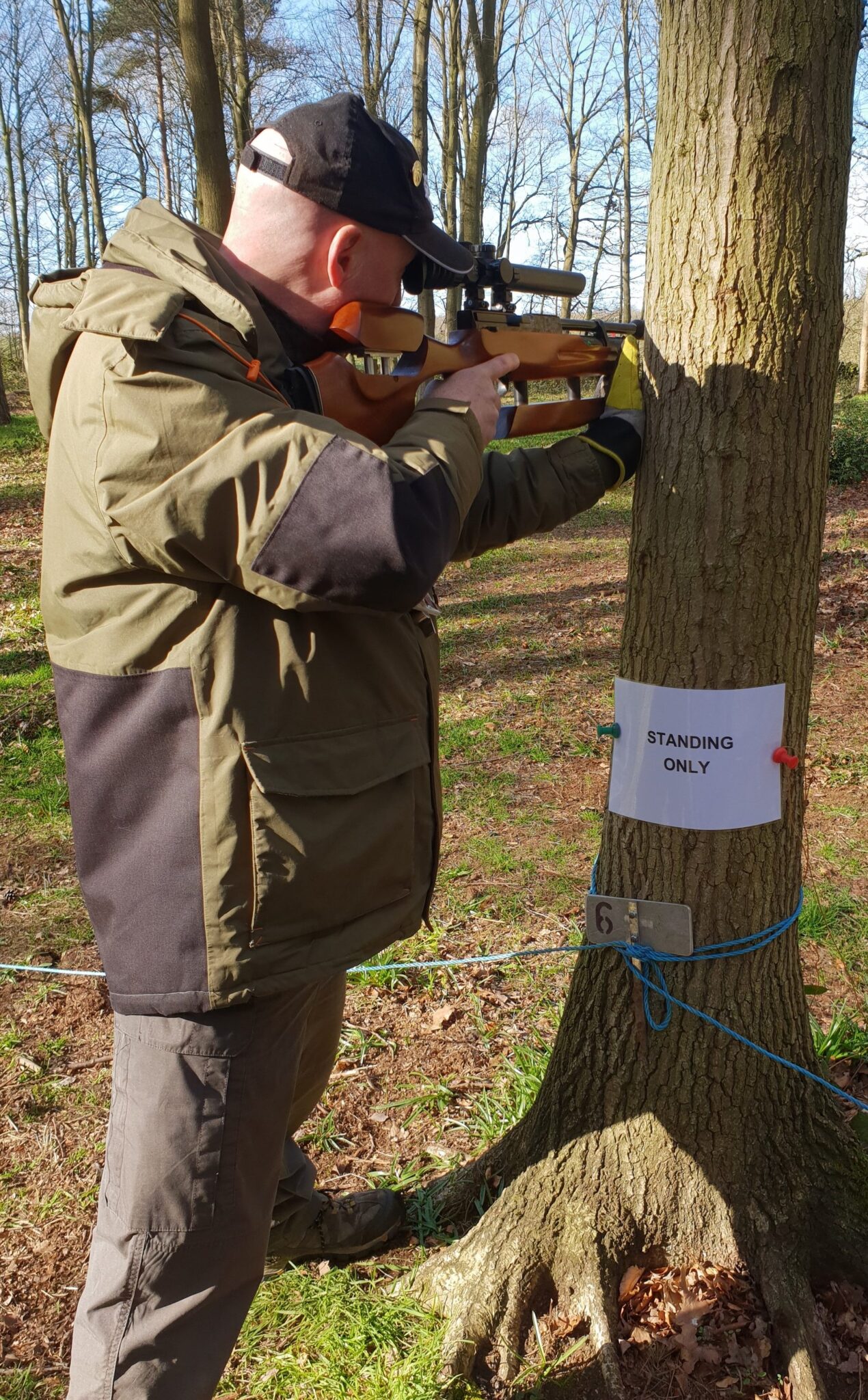 Airgun shooter taking a compulsory standing shot beside a tree on a hunter field target course