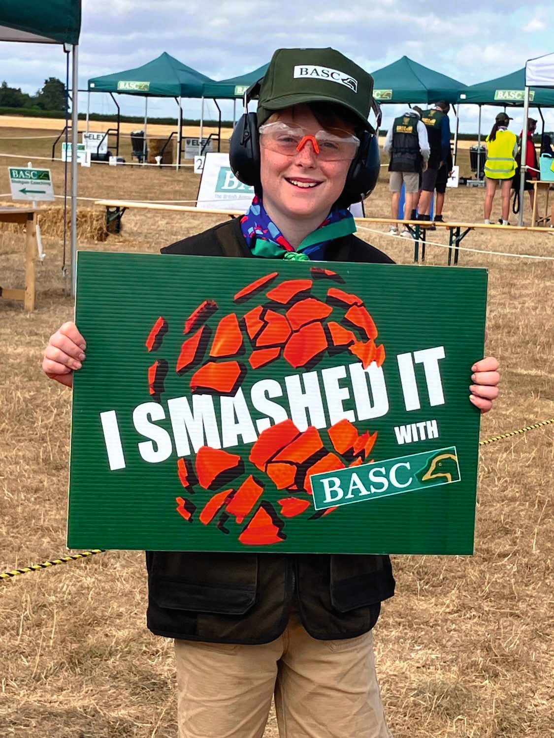A young Scout in ear defenders and safety glasses holding an I Smashed It board