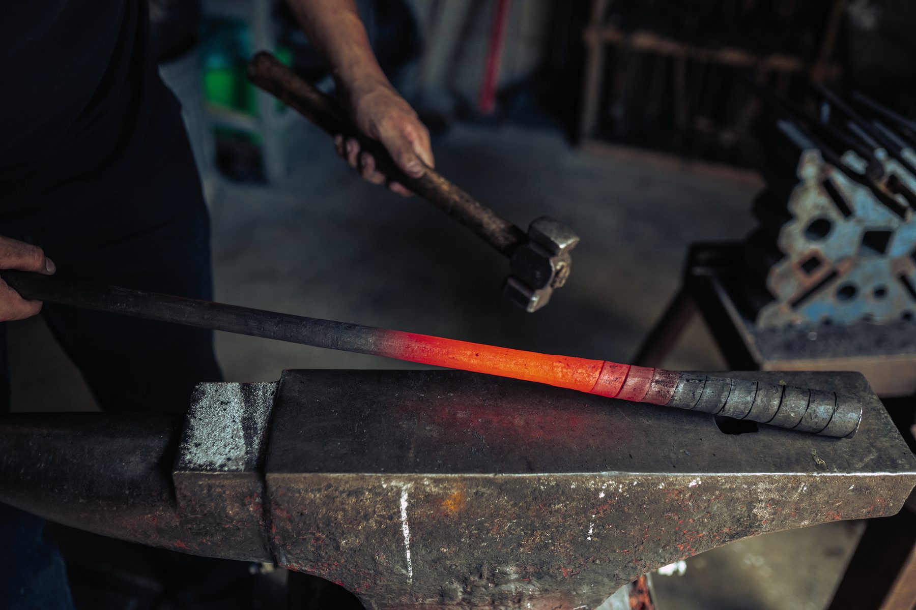 A glowing coiled barrel tube being forge welded with a hammer on the anvil