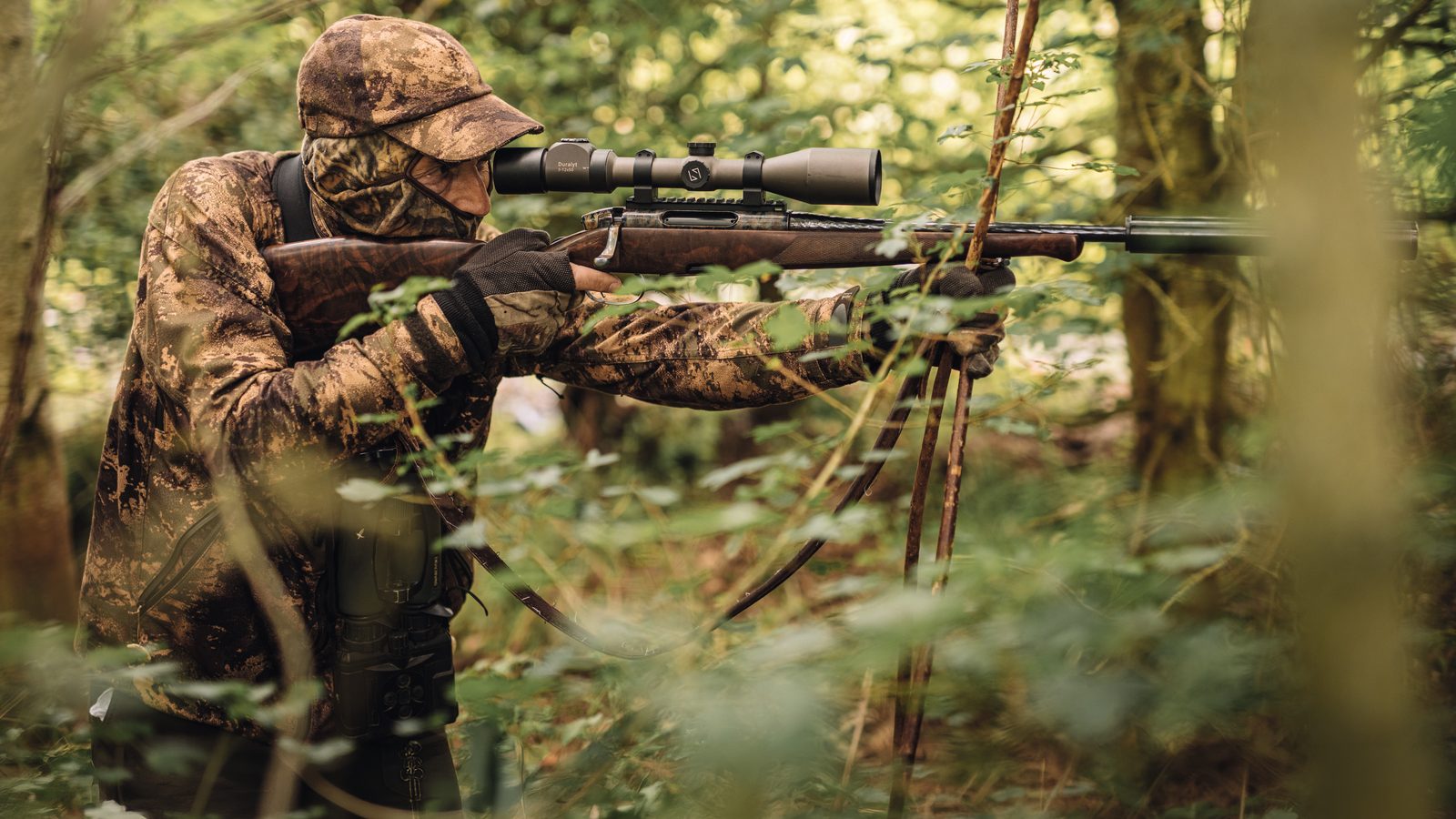 Graham Downing in camouflage taking aim with his rifle through woodland on a muntjac stalk