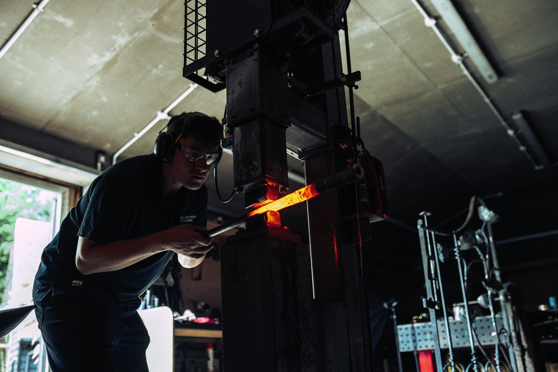 Toby Smith feeding a glowing barrel tube under a power drop hammer