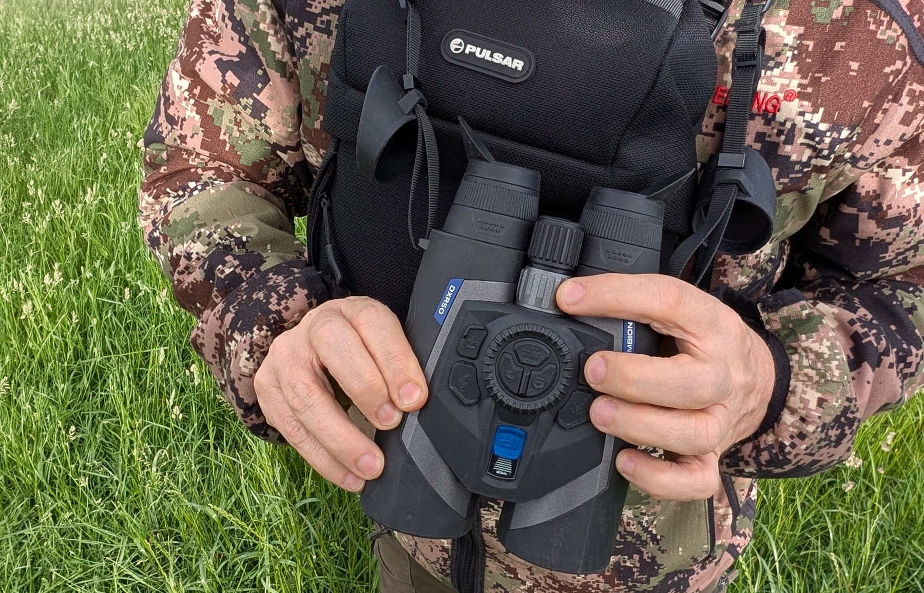 The Pulsar Symbion LRF DXR50 held in both hands in the field, with the controls under the fingertips
