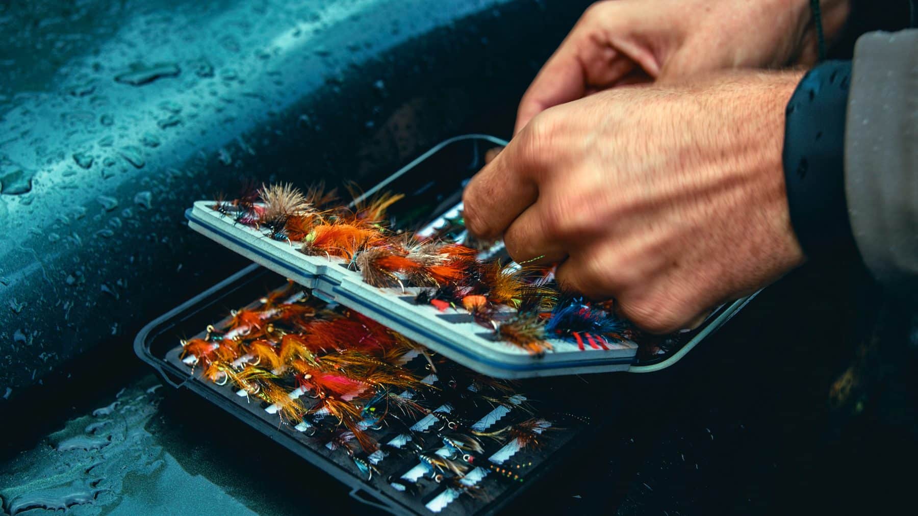 An angler selecting a fly from an open fly box on the riverbank at Benmore Estate