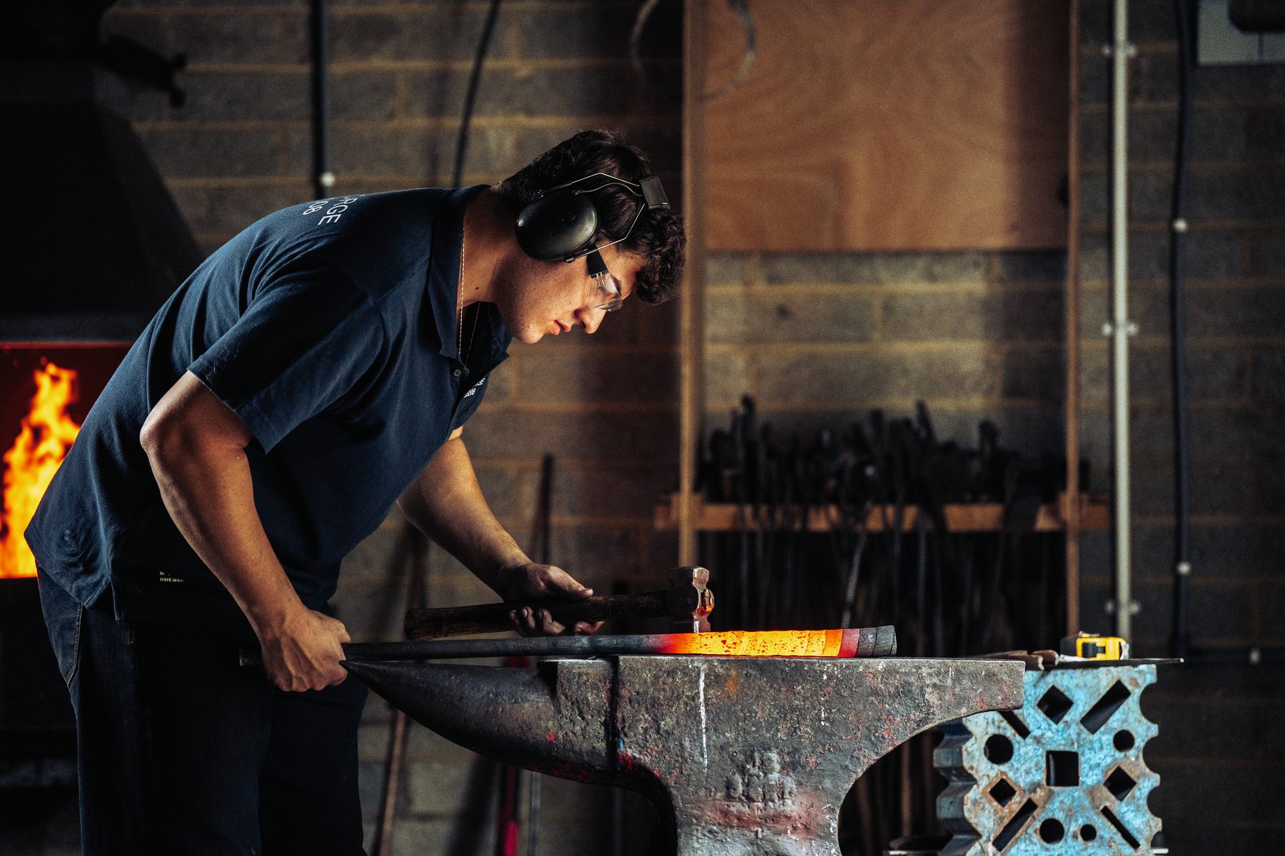 Blacksmith Toby Smith bent over a glowing bar on the anvil in his forge