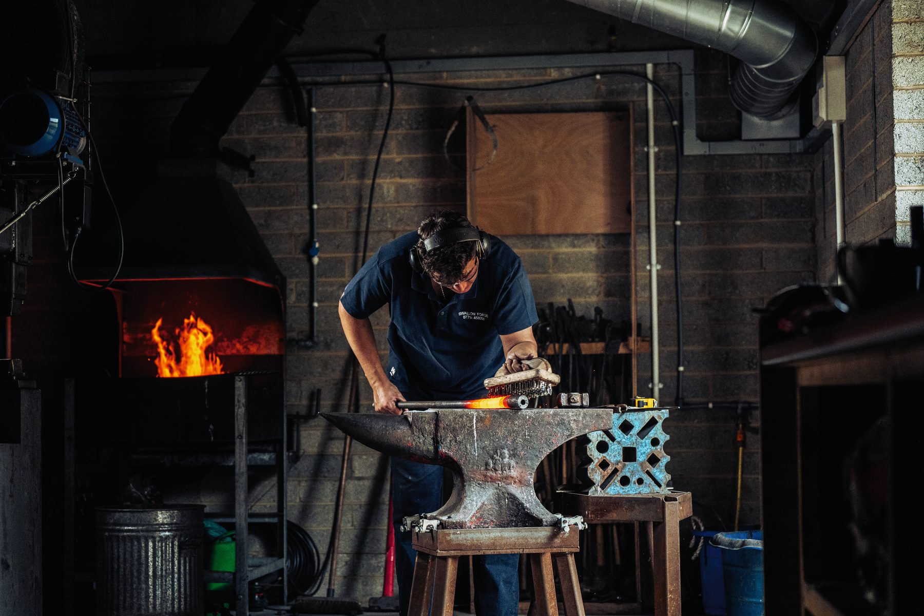 Toby Smith working a barrel tube with a wire brush at the anvil