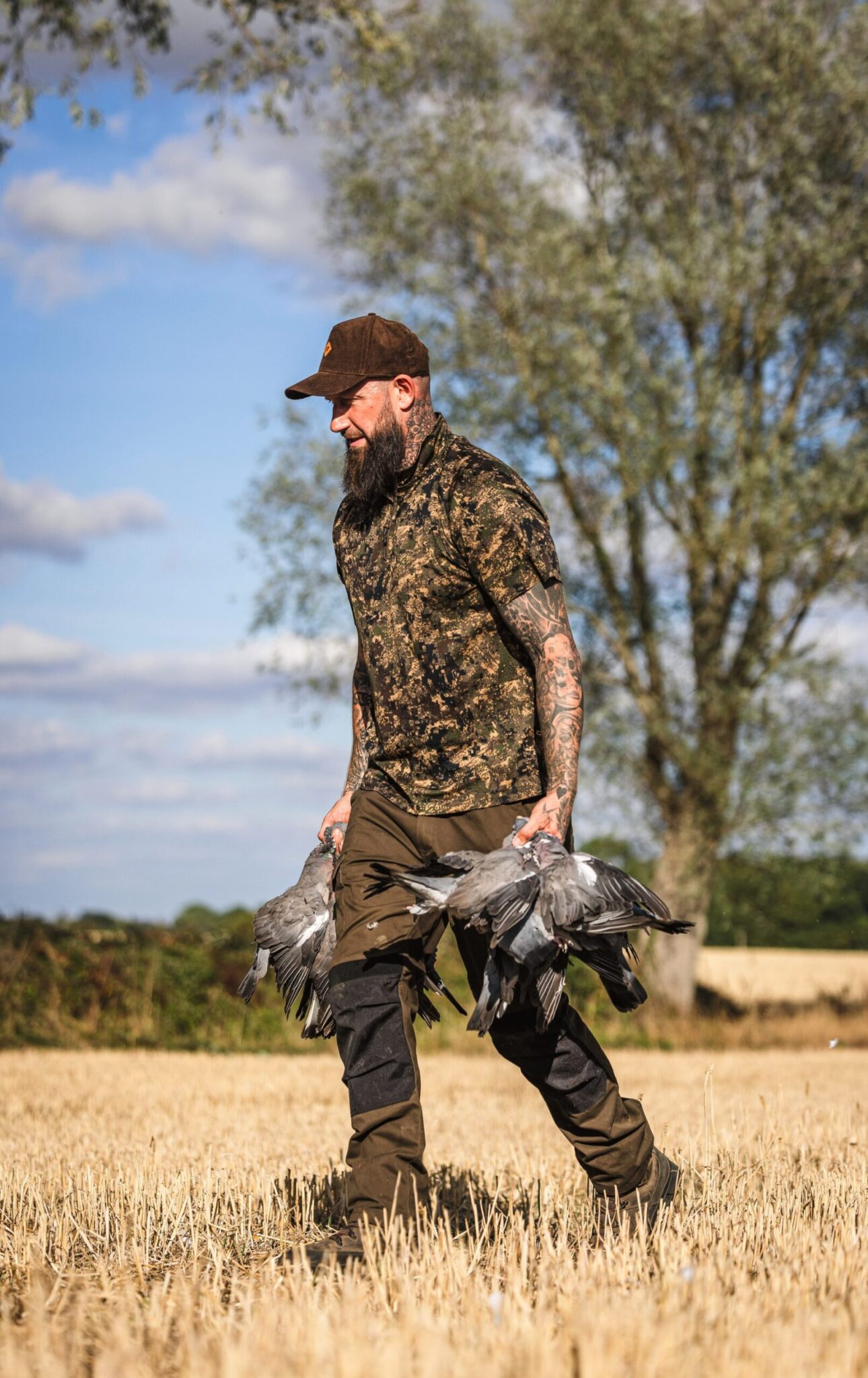 Dan Thor walking across wheat stubble carrying a bunch of shot pigeons in each hand