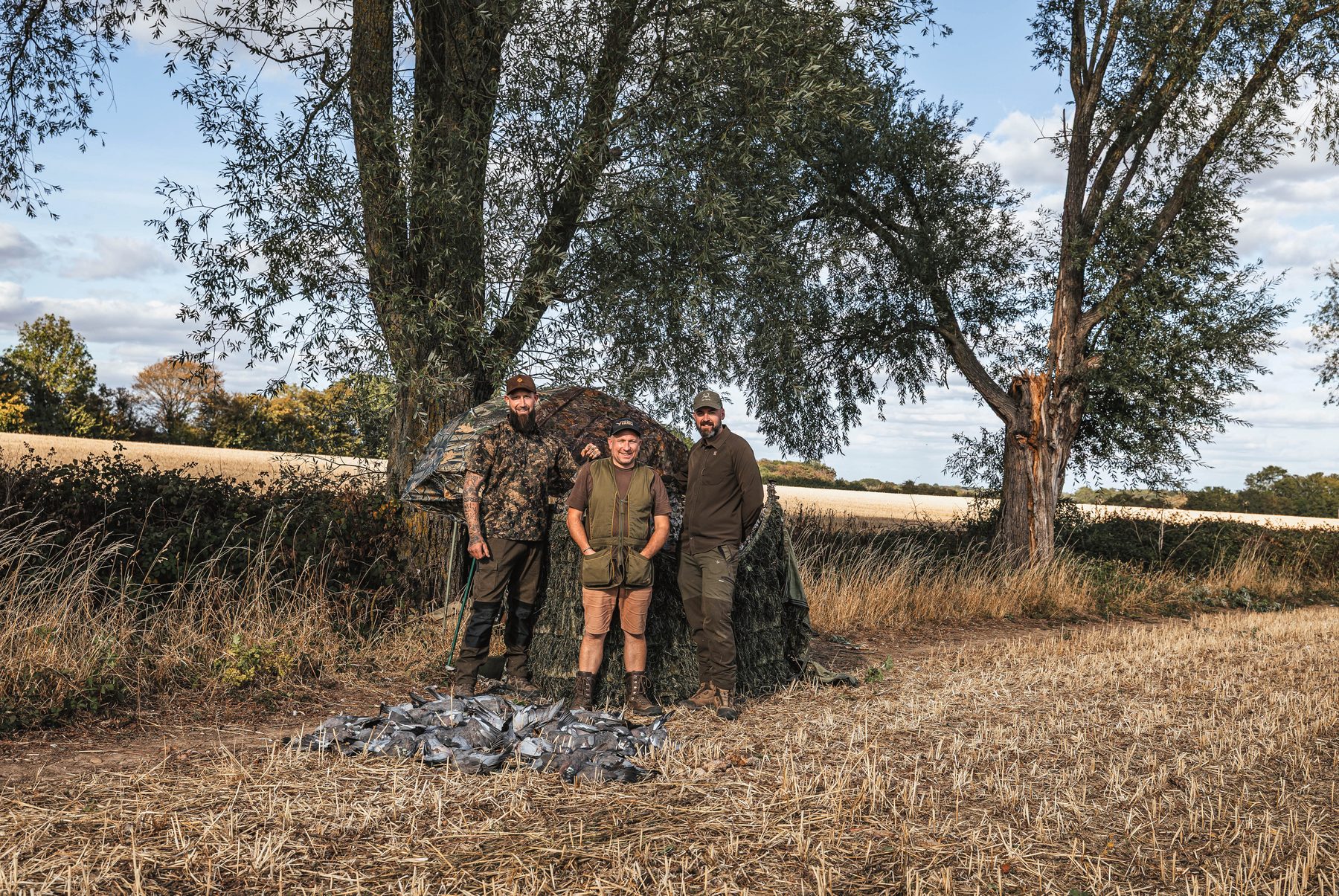 Dan Thor, James Elliott and Matt Kidd standing by their hide with the bag of pigeons laid out on the stubble